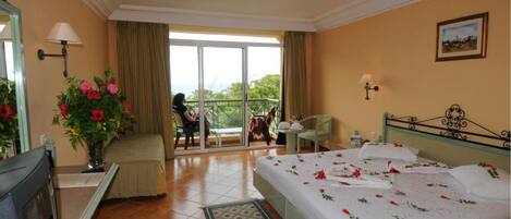 Habitación de hotel con cama, escritorio, silla, balcón con vistas y ventana con cortinas.
