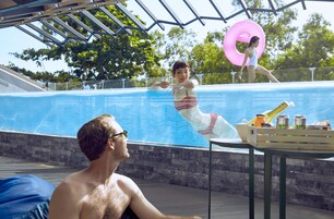 Zona de piscina con una persona en traje de baño, una silla de descanso y una mesa con bebidas y aperitivos.