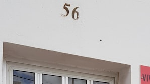 En vit dörr med en glasruta, siffran ’56’ ovanför och en röd skylt med bokstaven ’V’ på.