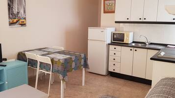 A compact kitchen with a refrigerator, microwave, and sink. There's a dining table with chairs and a small TV on a stand.