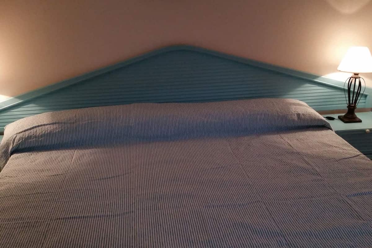 Een slaapkamer met een bed, nachtkastje en lamp.