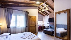 Een hotelkamer met een groot bed, een bureau, een open haard en een spiegelwand.