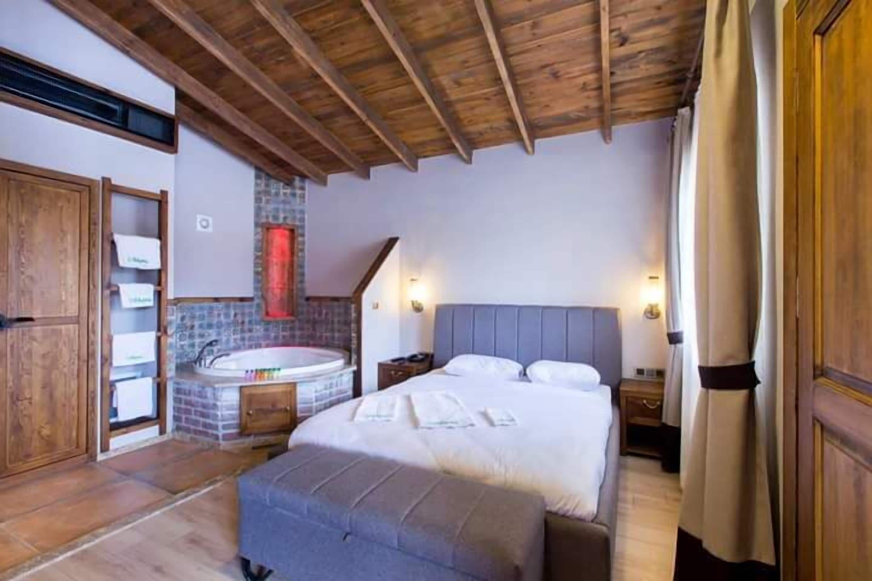 Un dormitorio con techo de madera, una cama grande, una bañera empotrada y un armario de madera.