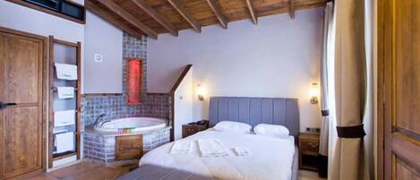 Un dormitorio con techo de madera, una cama grande, una bañera empotrada y un armario de madera.
