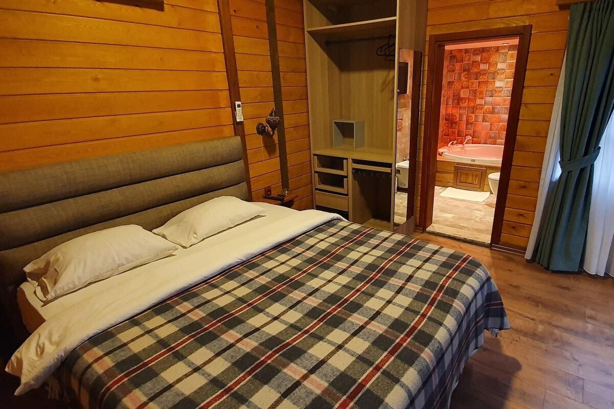 Een slaapkamer met een bed, een houten garderobe, een klein bureau en een badkamer zichtbaar door een open deur.