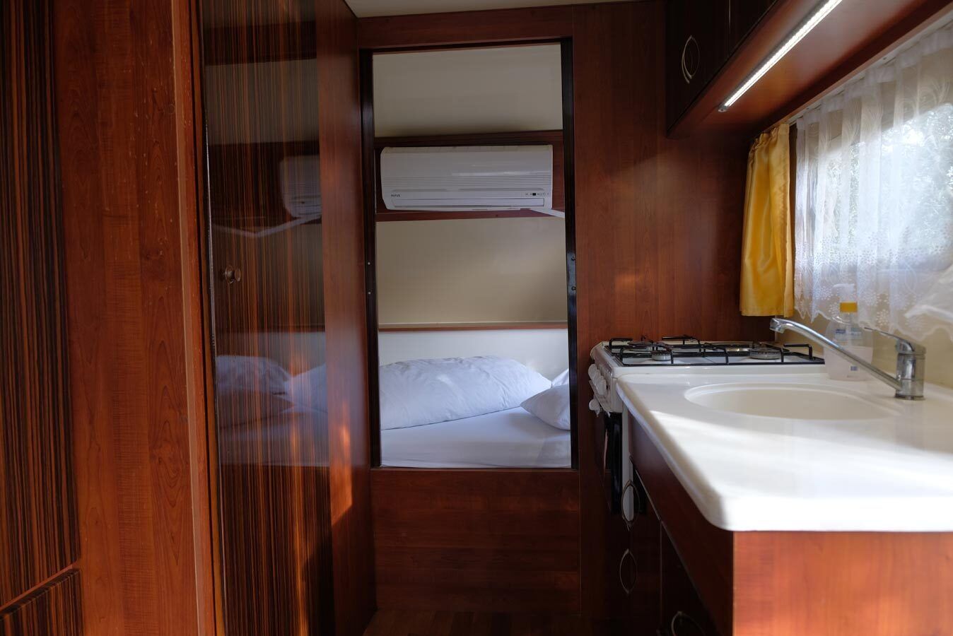 Une petite cuisine équipée comprenant un évier, une cuisinière et un petit lit avec du linge de lit blanc.