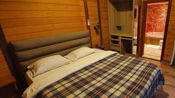 A bedroom with a large bed, a wooden headboard, a small desk, and a bathroom visible through an open door.