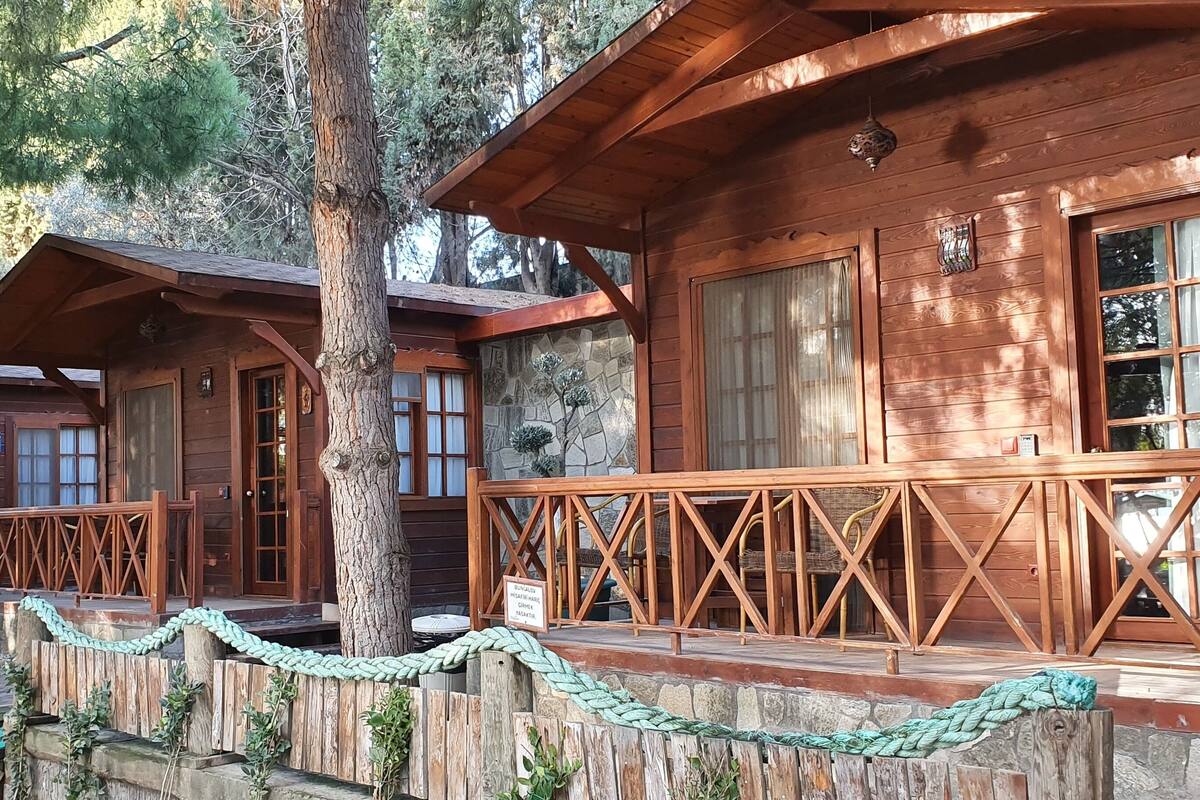 Una cabaña de madera con base de piedra, barandillas de madera y una pared de piedra cubierta de vegetación.