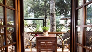 Een terras met houten tafels en stoelen, een plant in pot en een strohoed op een van de tafels.
