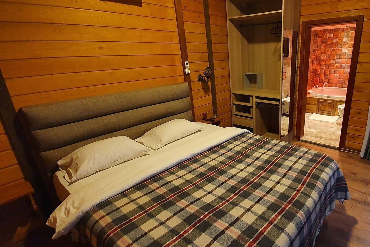 Un dormitorio con una cama grande, cabecera de madera, un escritorio pequeño y un baño visible a través de una puerta abierta.