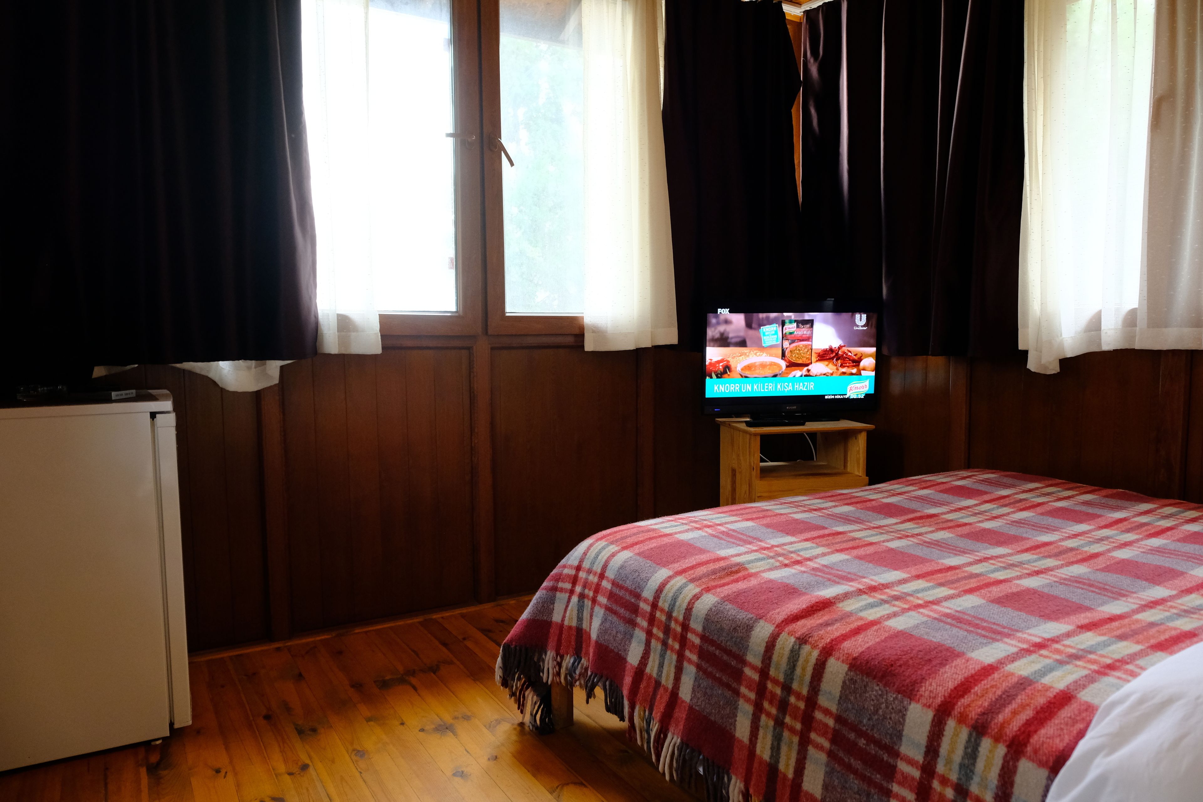 Ett rum med en säng, en tv på ett träställ och ett fönster med gardiner.