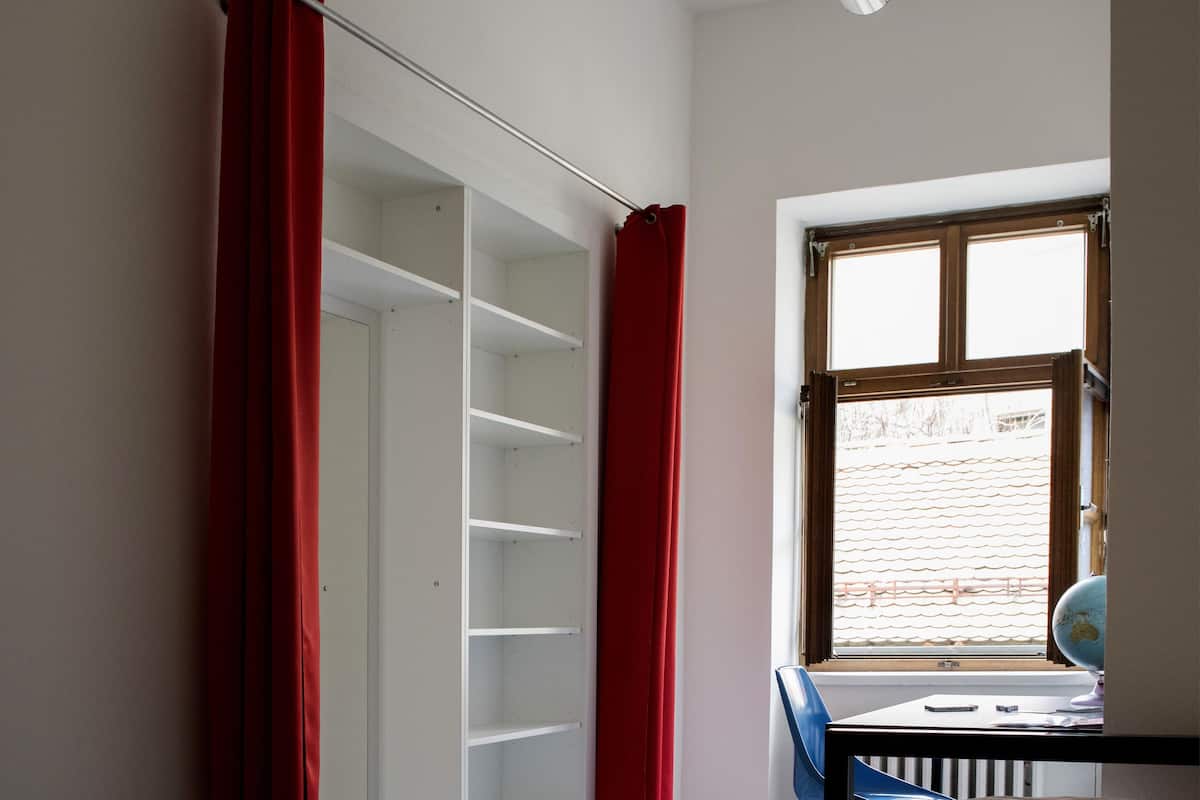 Quarto com cama, guarda-roupa, escrivaninha com cadeira e janela com persianas.