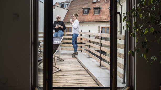 Eine offene Tür führt zu einem Balkon mit Blick auf Gebäude und ein Kirchturm.