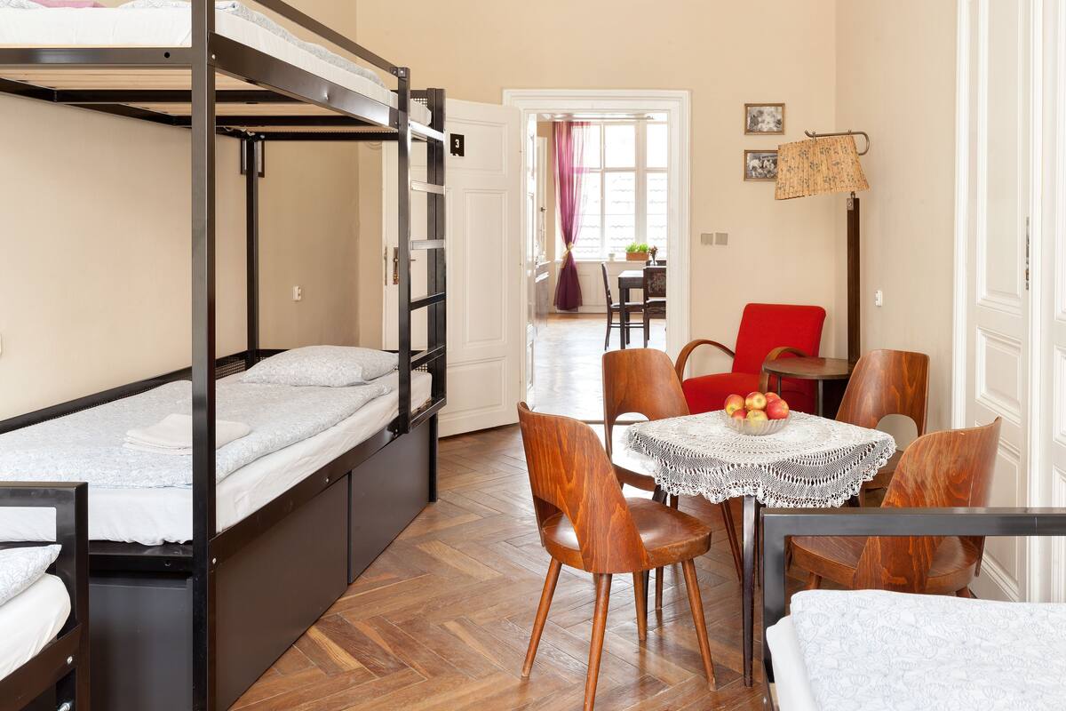 Une chambre de dortoir avec des lits superposés, une table à manger avec des chaises et un petit coin cuisine.