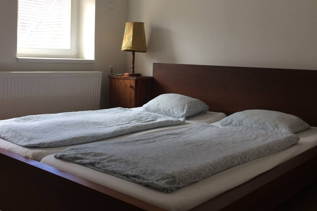 Une chambre à coucher avec un grand lit, une table de chevet avec une lampe et une fenêtre avec des stores.