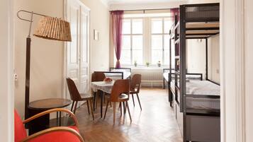 A room with a bunk bed, a dining table with chairs, a lamp, and a window with curtains.