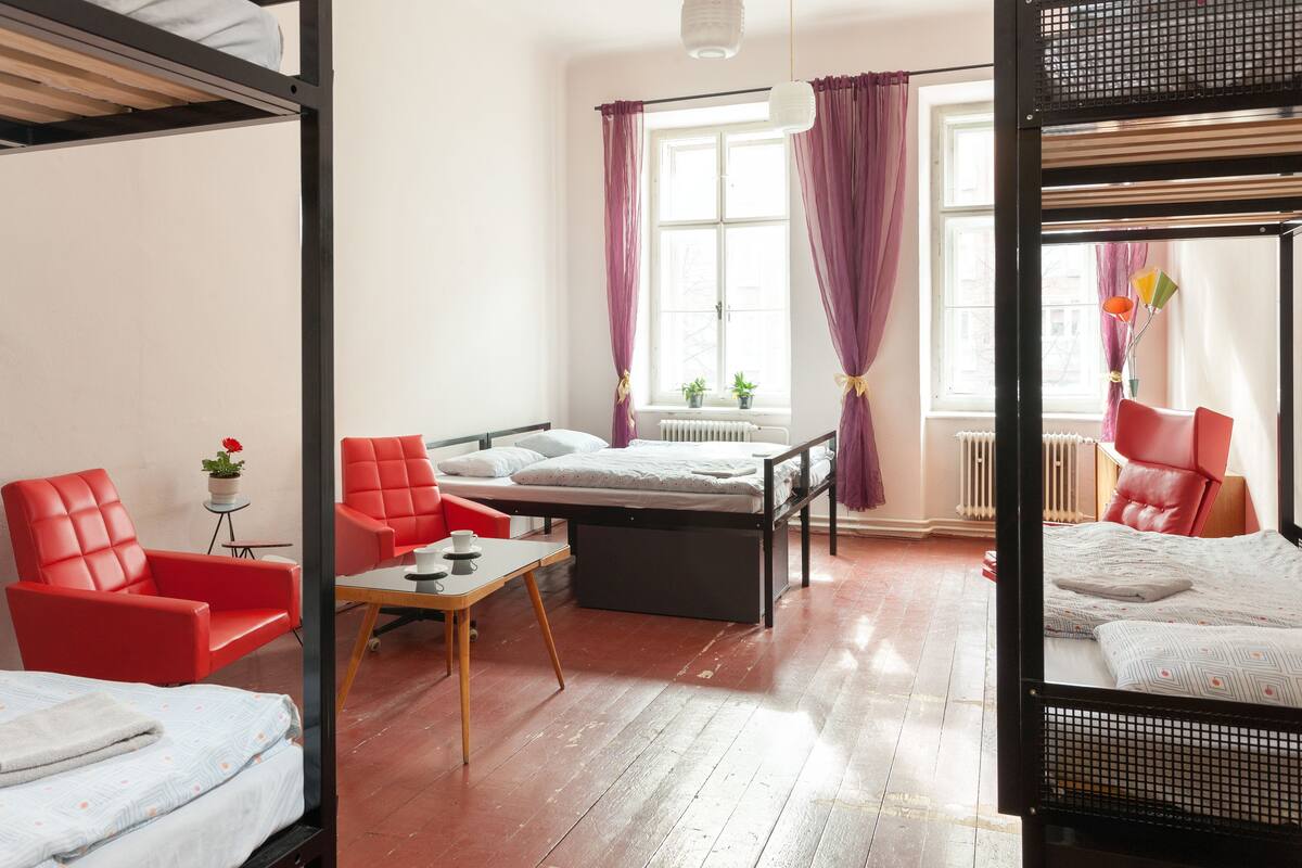 Une pièce avec des lits superposés, une chaise rouge, une petite table et une fenêtre avec des rideaux.