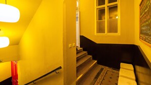 Un escalier avec une rampe noire, une fenêtre à vitres dépolies et un mur sur lequel est fixé un tableau noir affichant du texte.