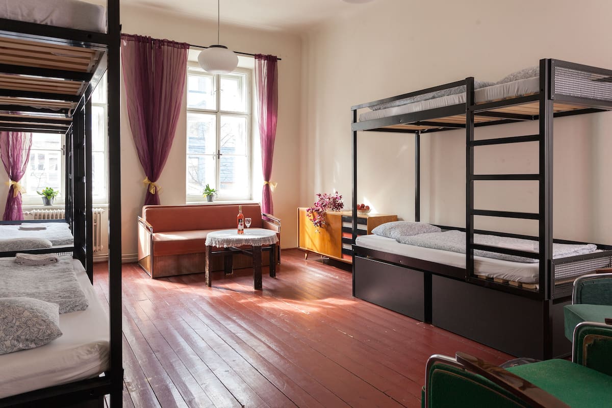 Une chambre de dortoir avec des lits superposés, un canapé, une petite table ronde et une fenêtre avec des rideaux.