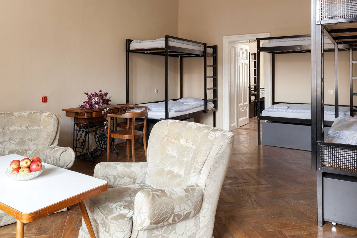 Une chambre de dortoir avec des lits superposés, une table à manger avec des chaises, un saladier rempli de fruits et une chaise à motifs floraux.