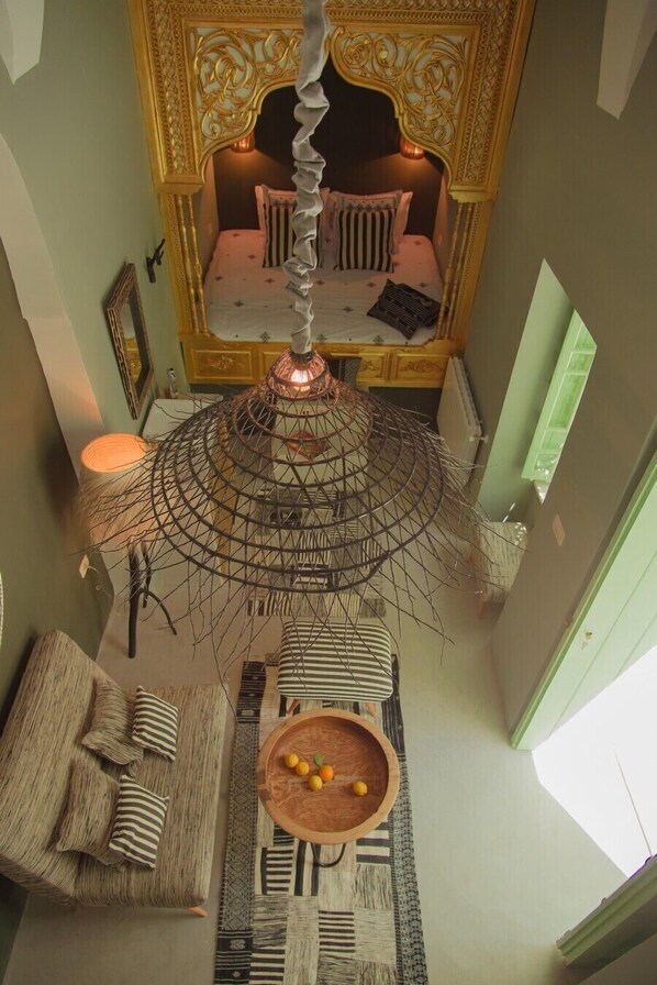 A room with a bed, a hanging chair, a table with fruits, and a decorative hanging lamp.
