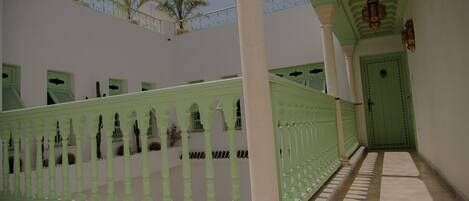 A corridor with a green railing, white columns, and a green door.