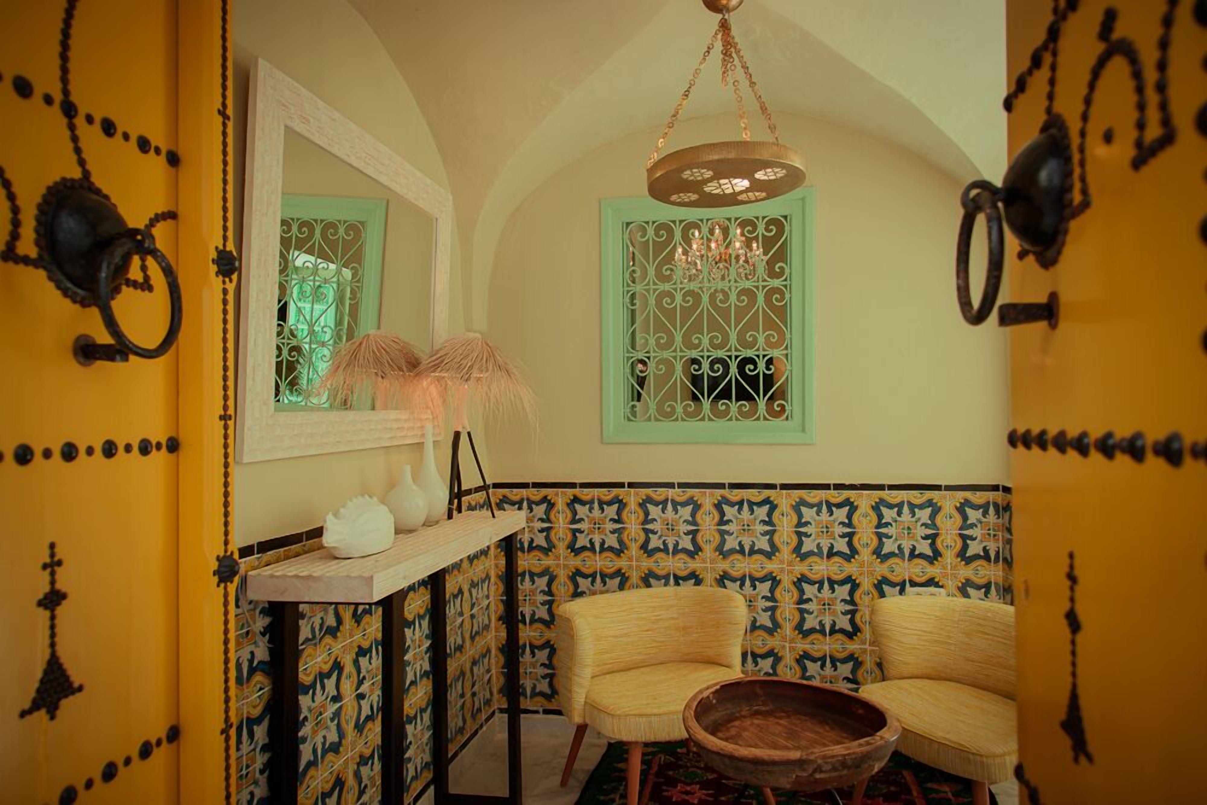 A room with a yellow door, a woven chair, a wooden bowl, and a mirror on the wall.