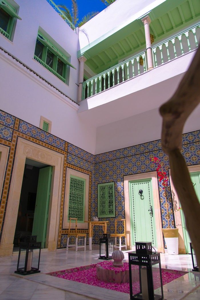 A courtyard with a tiled floor, a central seating area with chairs, and a balcony with a railing.