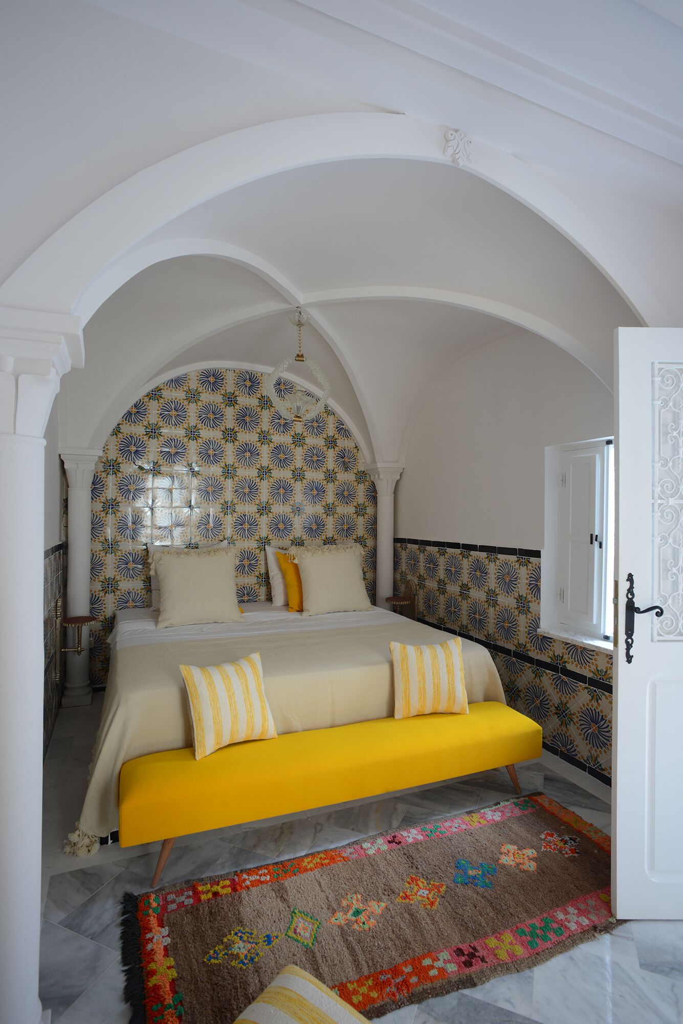 Un dormitorio con una cama bajo un techo abovedado, papel tapiz estampado y una alfombra colorida.