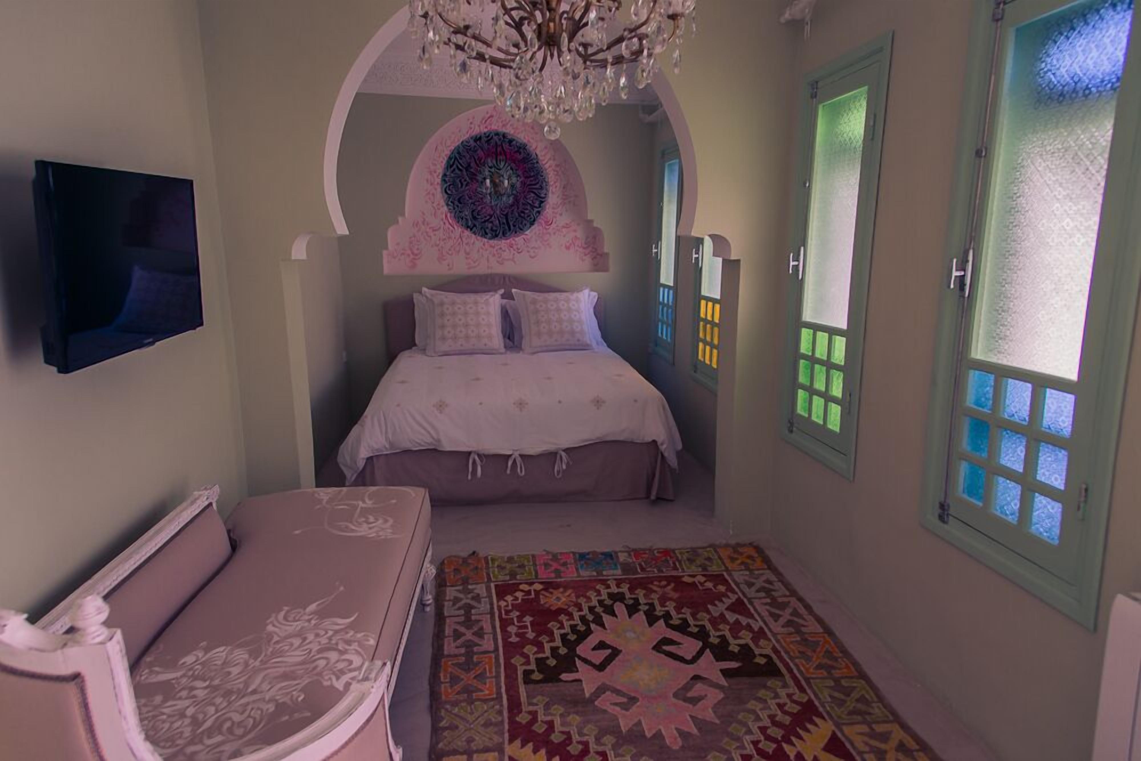 Un dormitorio con cama, televisor, candelabro y alfombra estampada.