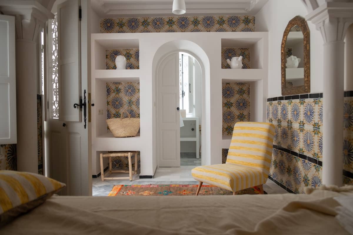 A bedroom with a bed, a chair, a small table, and a wardrobe.