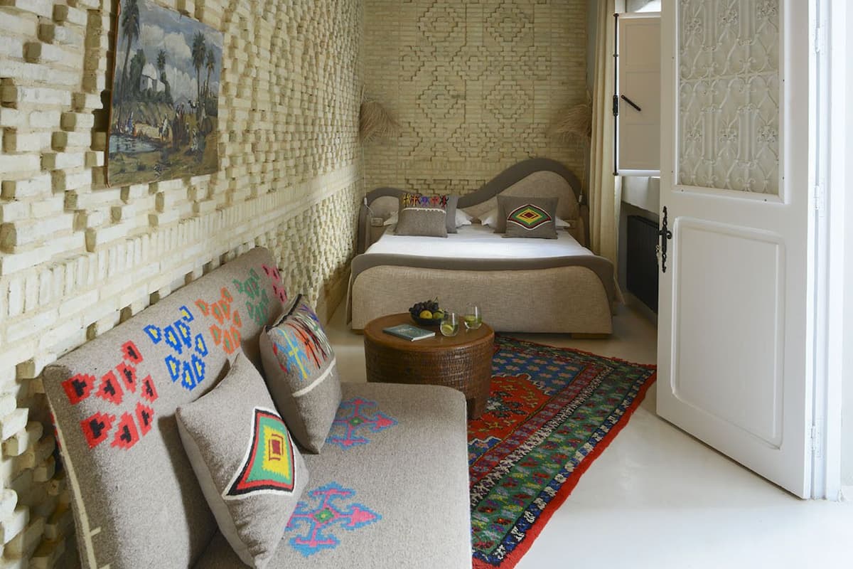A cozy bedroom with a patterned brick wall, a bed with a headboard, a hanging light fixture, and a colorful rug.