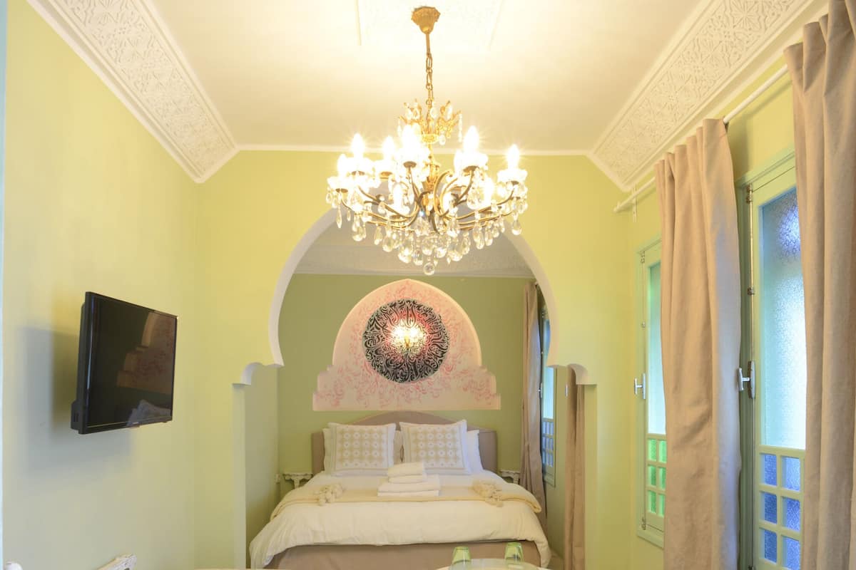 A bedroom with a bed, a TV, a chandelier, a patterned rug, and a sofa.