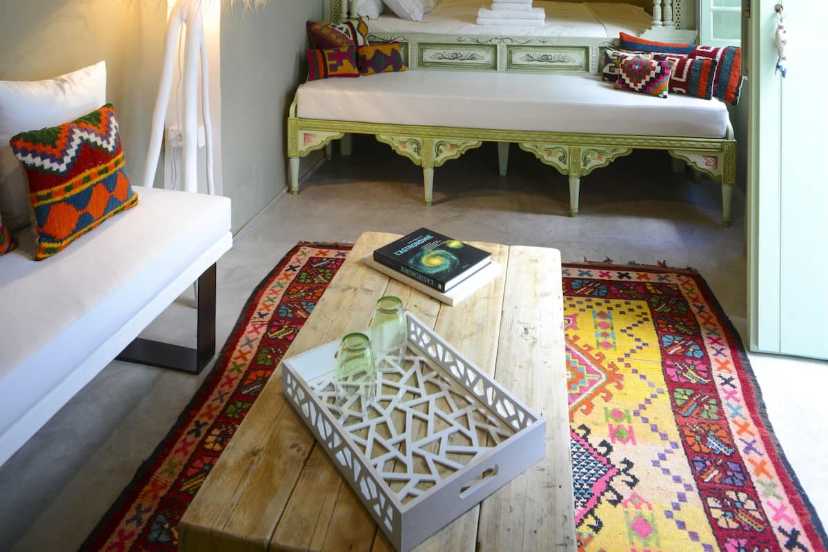 A room with a bed, a sofa, a lamp, a coffee table, and a patterned rug.
