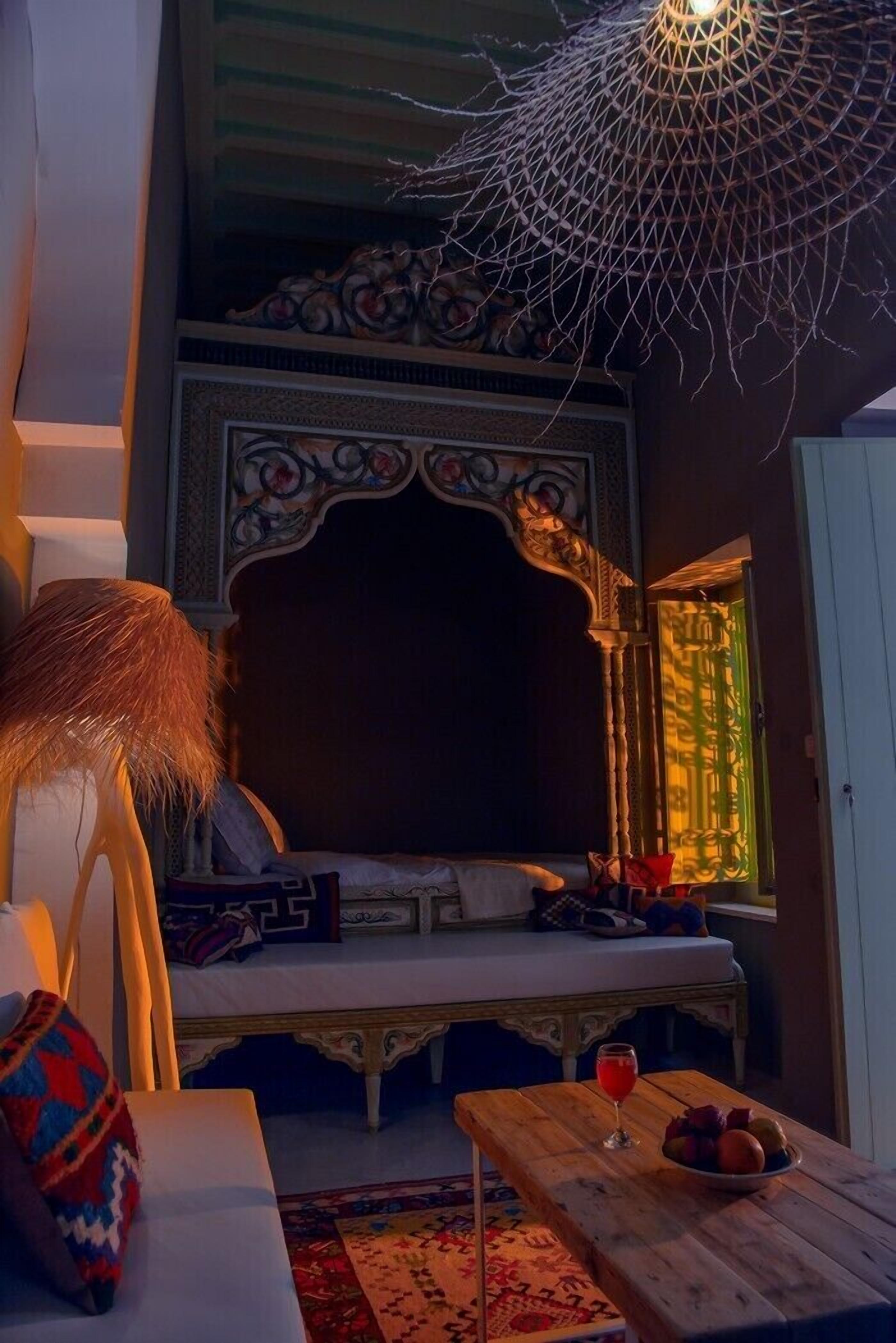 Una habitación acogedora con una cama, una mesa con fruta y una bebida, y una lámpara colgante decorativa.