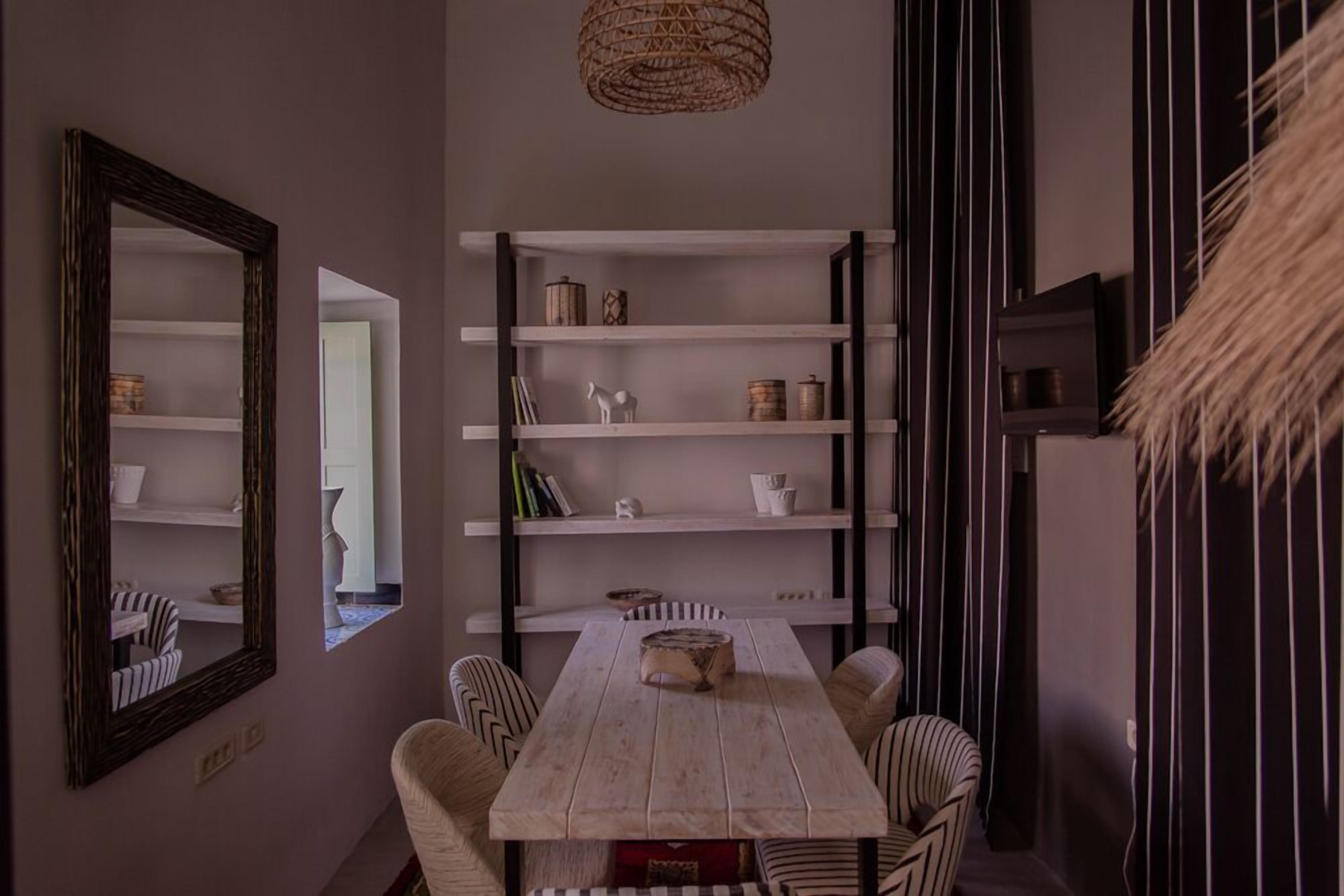 A dining area with a wooden table and striped chairs, a white bookshelf with decorative items, and a large mirror on the wall.