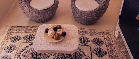 A bedroom with a bed, two wicker chairs, a small table with decorative items, and a patterned rug.