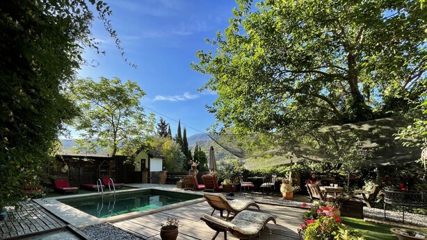 A pool area with a wooden deck, lounge chairs, and a small building in the background. - Fundalucia (Quentar)