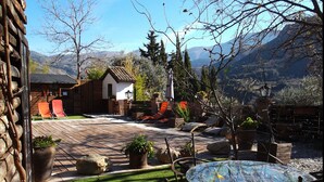 A patio with a glass table and chairs, surrounded by potted plants and a small wooden structure. - Fundalucia (Quentar)