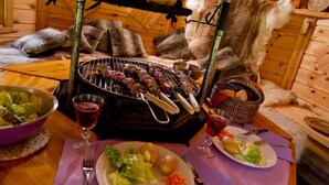 Un intérieur rustique en bois, avec un barbecue, un saladier rempli de salade et un panier de pain.