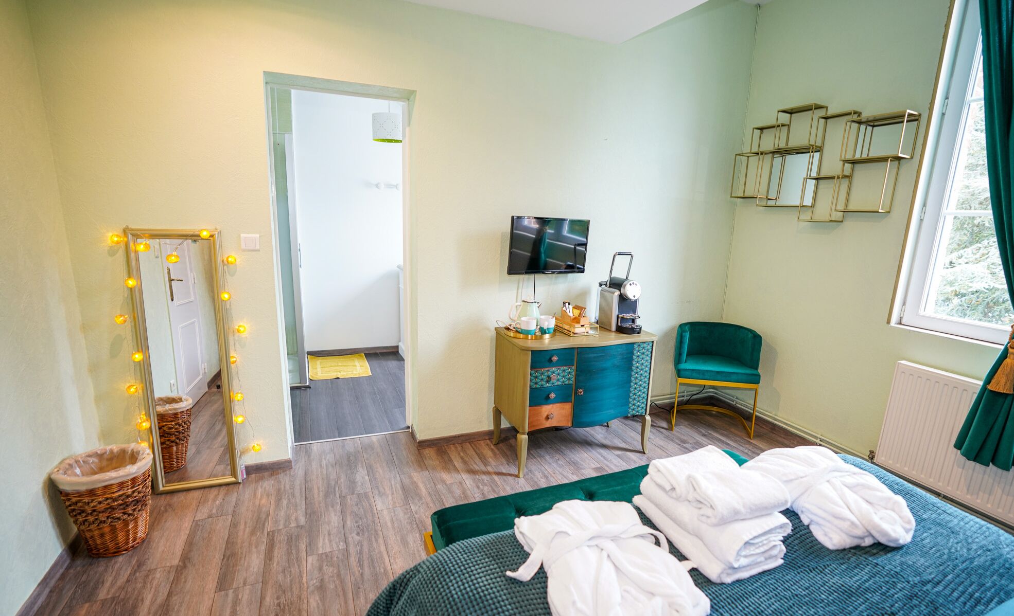A hotel room with a bed, a vanity with a mirror, a television, a coffee machine, and a chair.