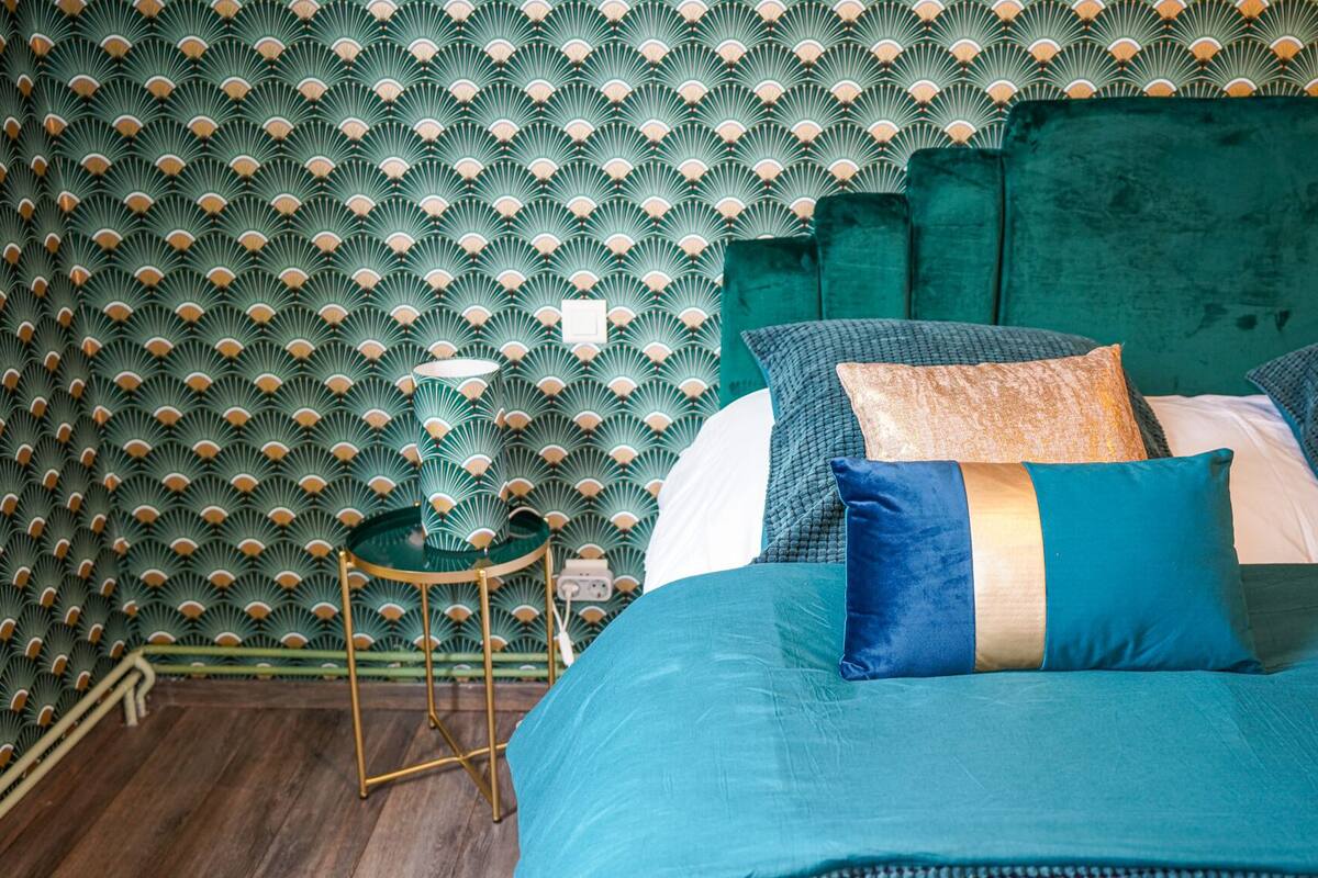Une chambre à coucher avec un papier peint à motifs, une tête de lit verte et plusieurs coussins.
