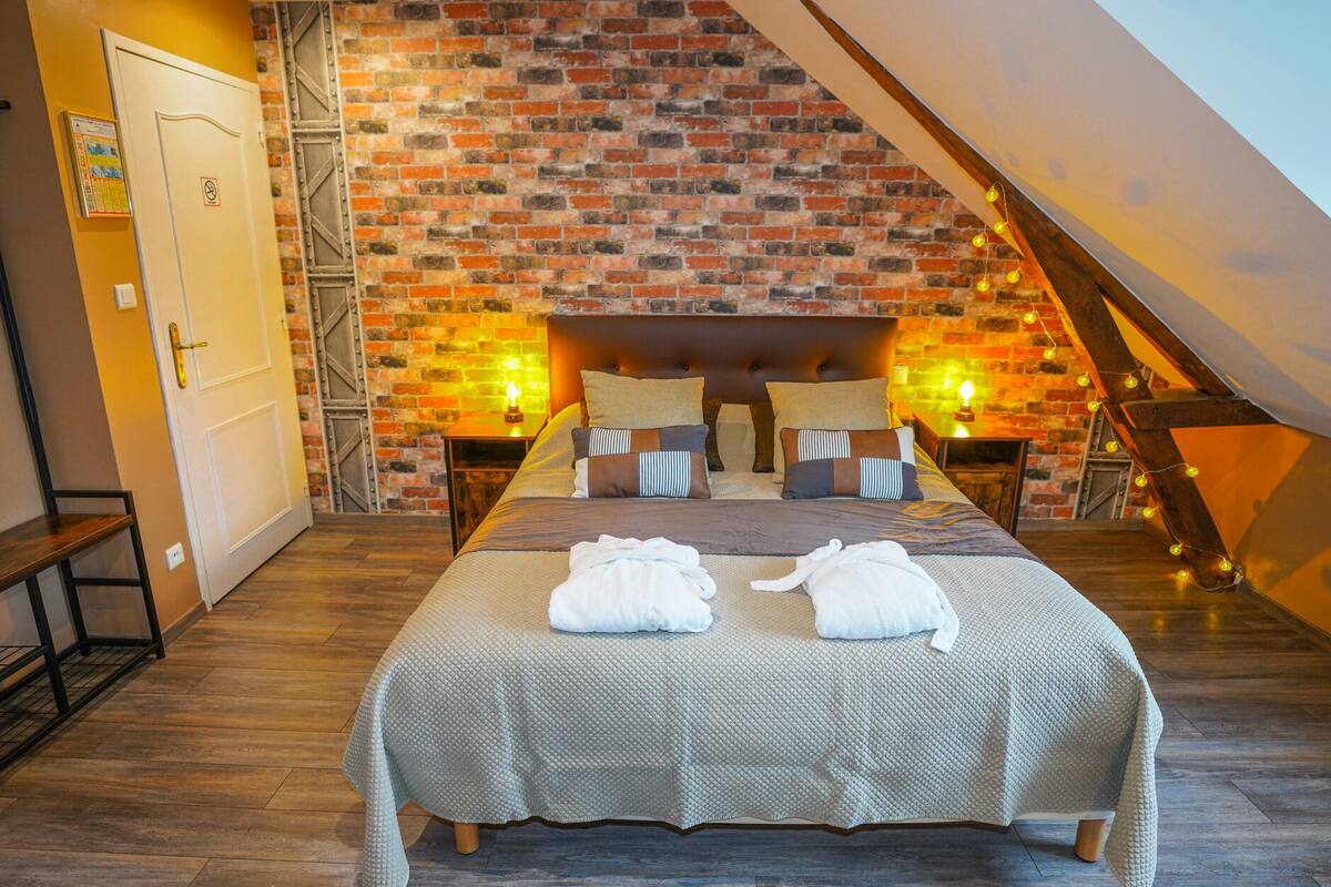 Une chambre avec un mur en briques, un plafond de style industriel et un lit avec deux serviettes blanches.