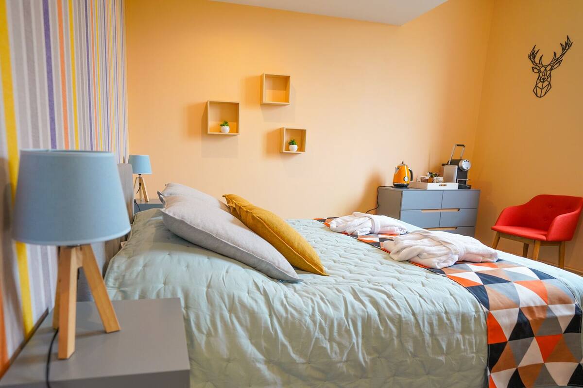 Une chambre à coucher comprenant un lit, des tables de chevet, un bureau, une chaise et une étagère murale agrémentée d’une plante.