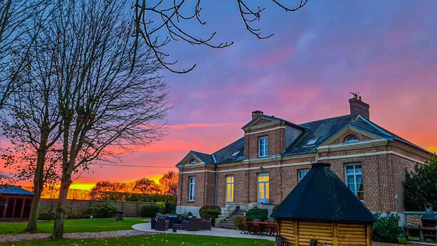 Une grande maison en briques, dotée d’une façade symétrique, d’une cheminée imposante et d’une pelouse bien entretenue.