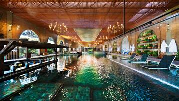 Piscina interior com teto de madeira e espreguiçadeiras nas laterais.