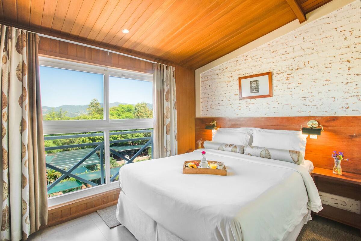 Un dormitorio con una cama grande, cabecera de madera y vista a un paisaje verde a través de una ventana.