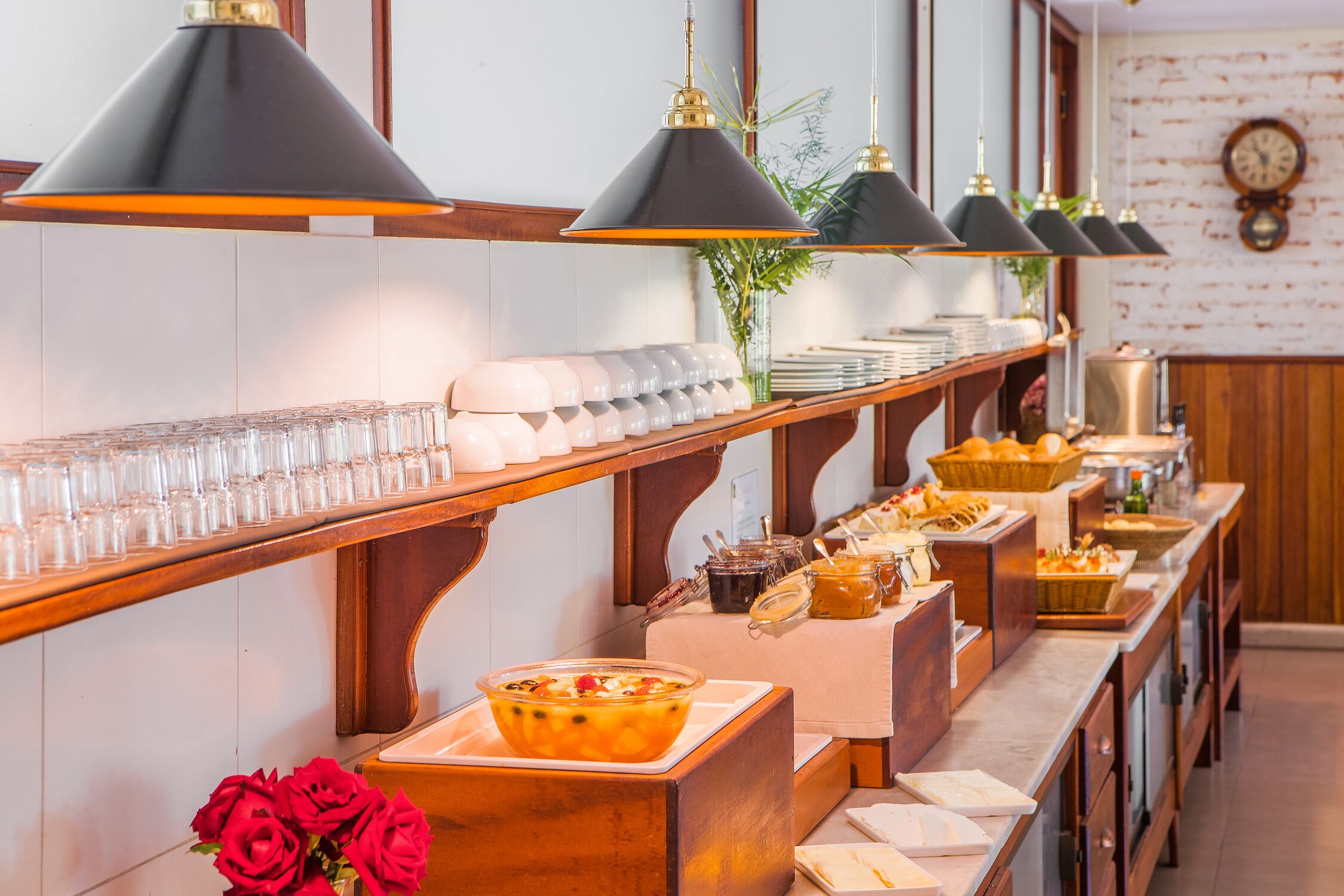 Disposição de buffet com várias estações de serviço, incluindo diversos pratos e bebidas, e um relógio na parede.