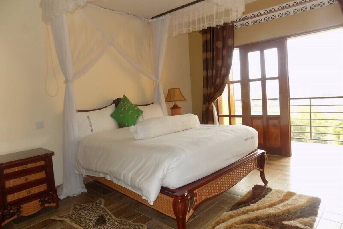 Uma cama com dossel e cortinas, roupa de cama branca, um travesseiro verde e um tapete com estampa de leopardo.