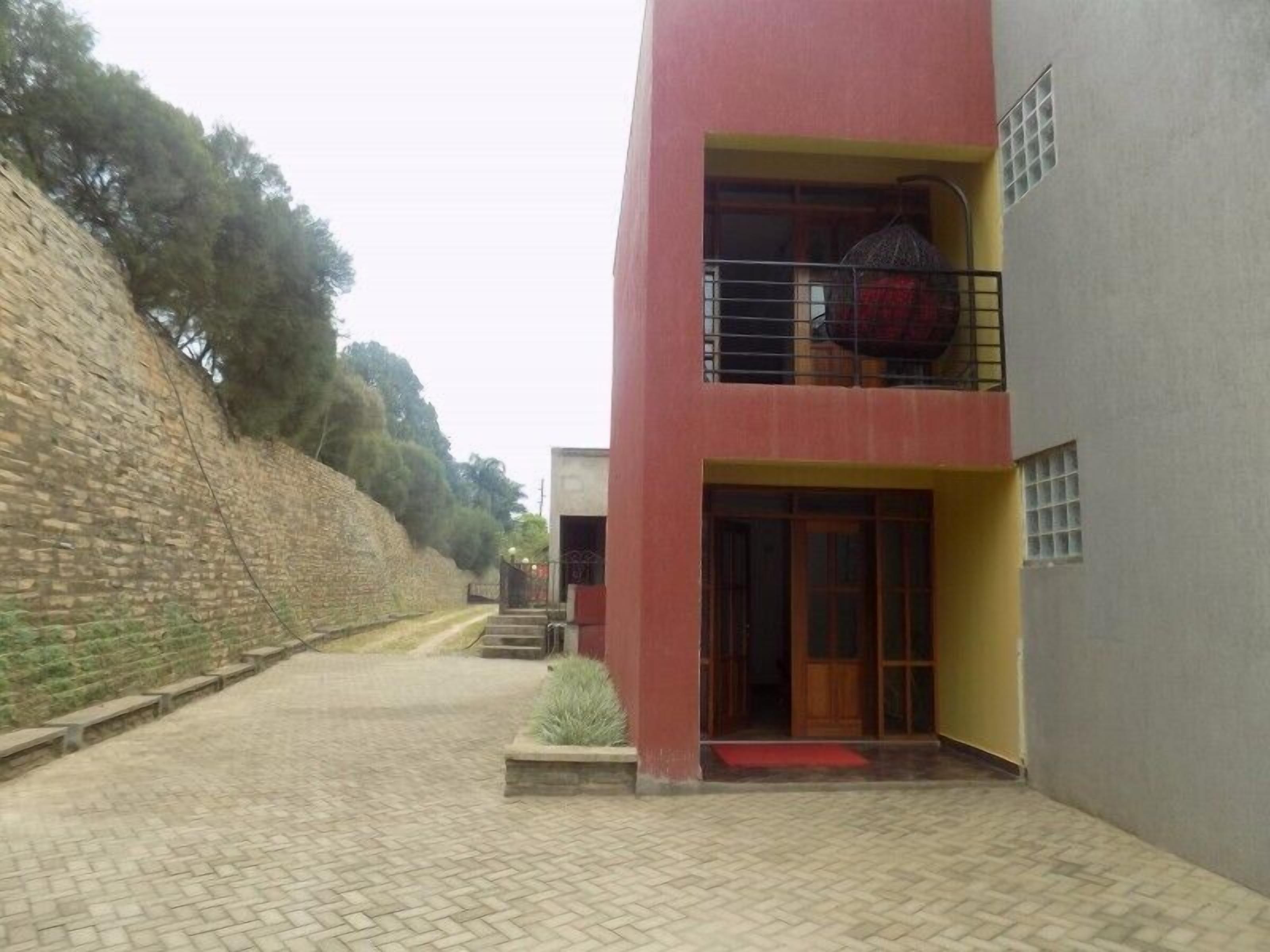 A building with a red and grey facade, a visible balcony, and a paved pathway leading to the entrance.
